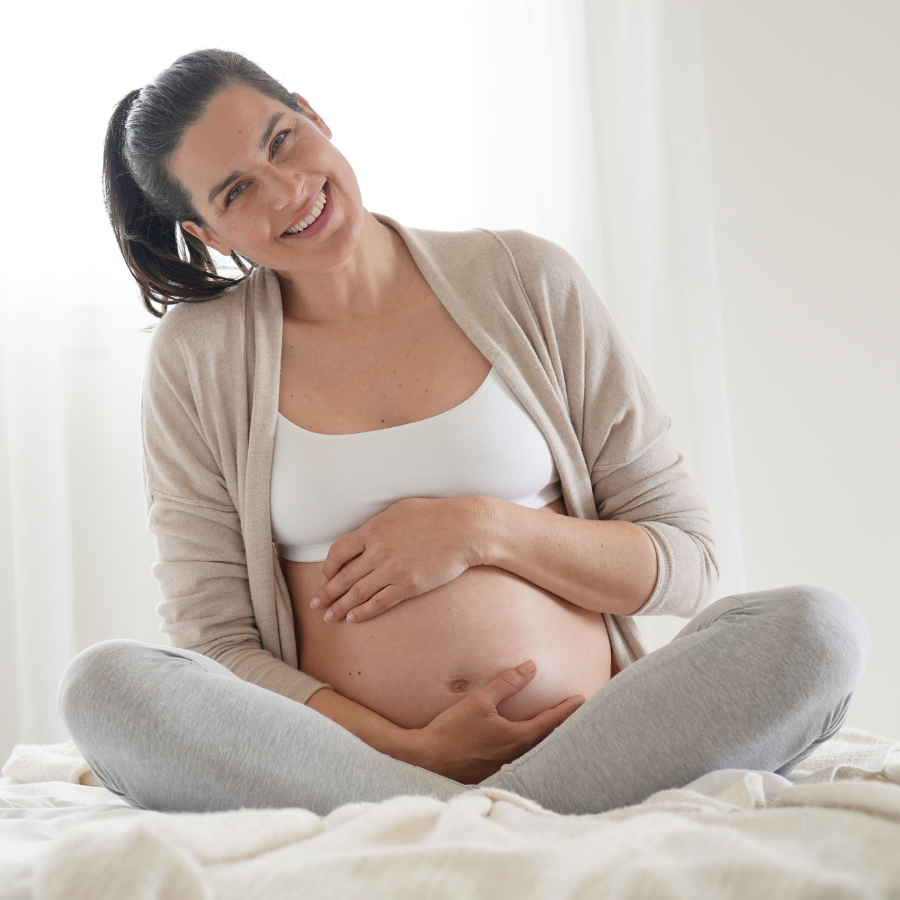 uśmiechnięta kobieta w ciąży siedząca na łóżku
